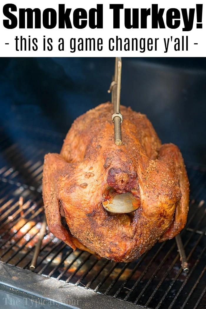 A whole smoked turkey, boasting crispy, golden-brown skin with visible seasoning, hangs on a metal hook inside a smoker. Text at the top reads, "Smoked Turkey! - This is the best smoked turkey—a game changer y'all!