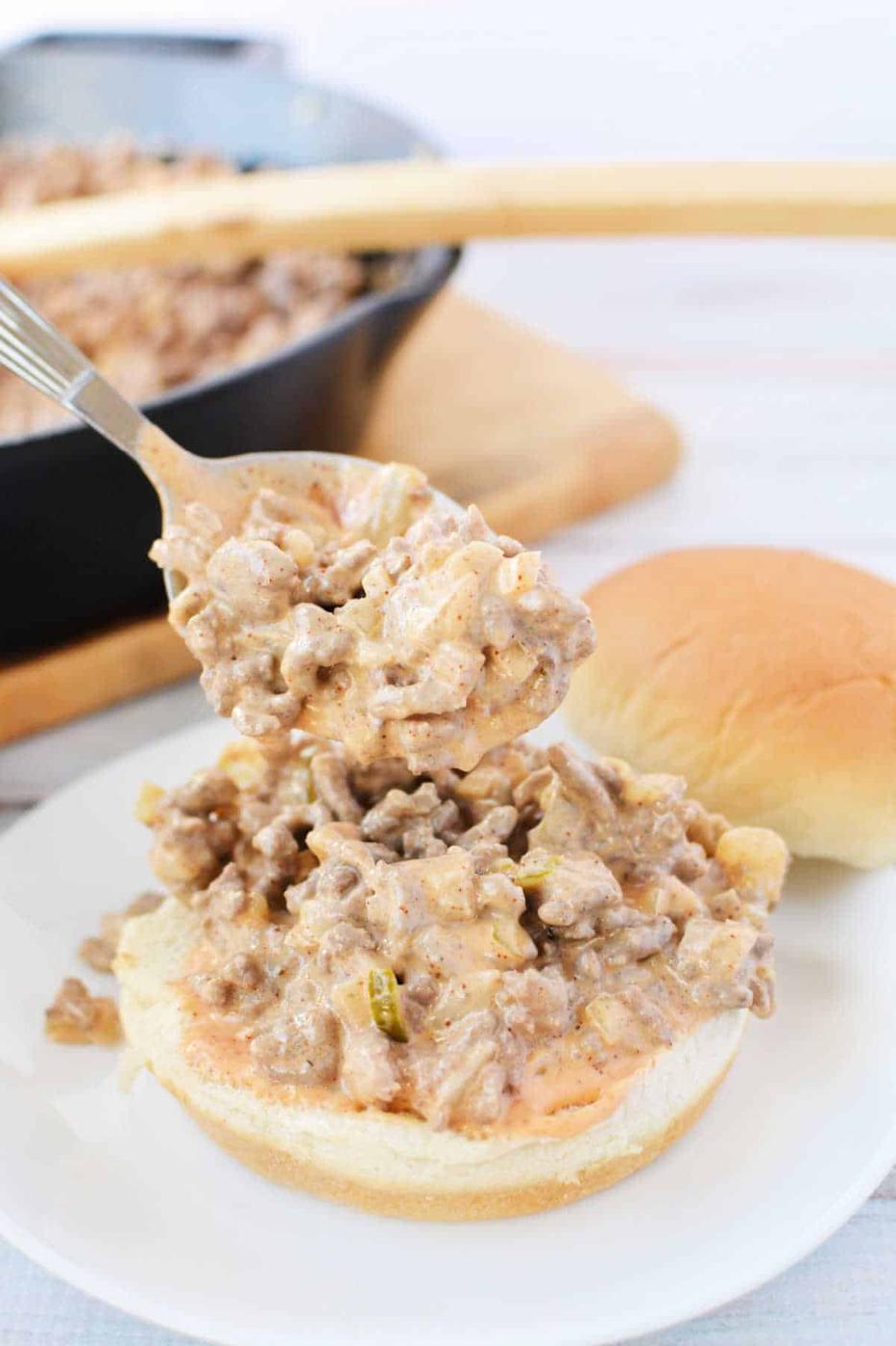 A spoon serving creamy Big Mac Sloppy Joes, with a skillet and more buns in the background.