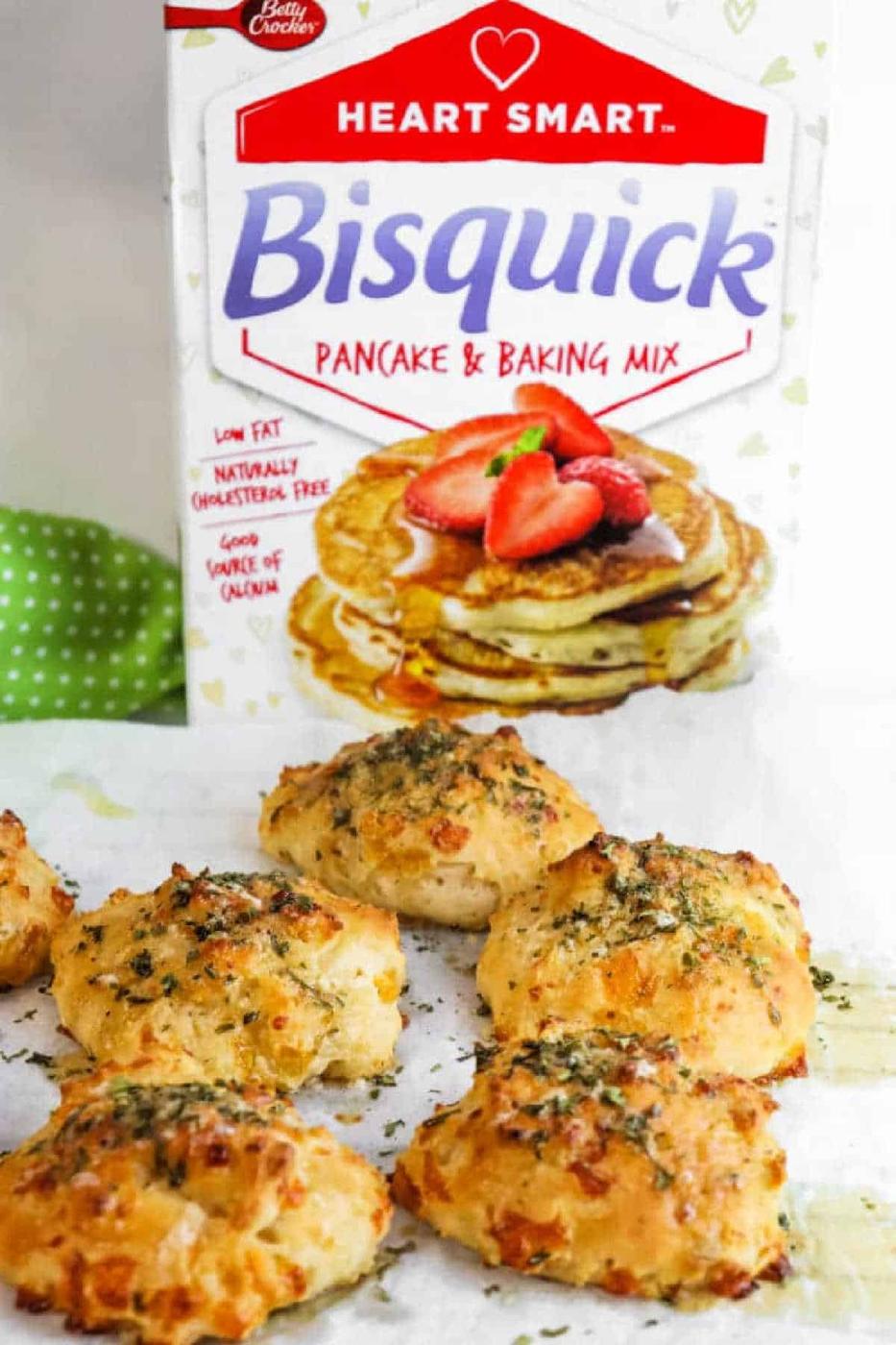 Golden cheese biscuits in front of a Bisquick Pancake & Baking Mix box, these tasty bisquick cheddar bay biscuits are topped with fresh herbs.