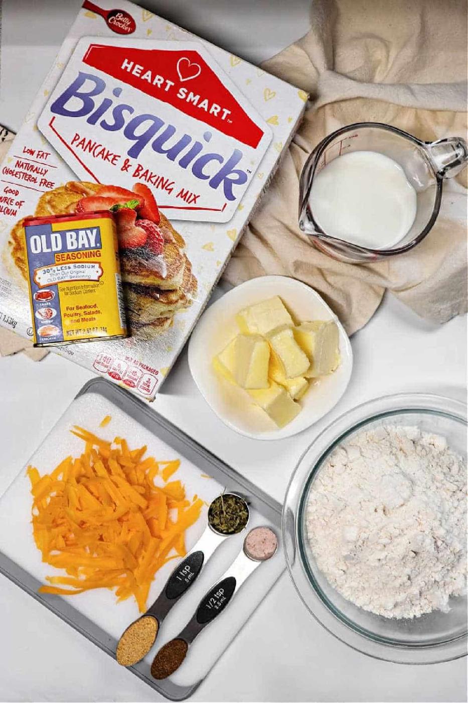 Bisquick cheddar bay biscuits ingredients—cheddar cheese, spices, butter, flour, and milk—are arranged on a counter for baking.