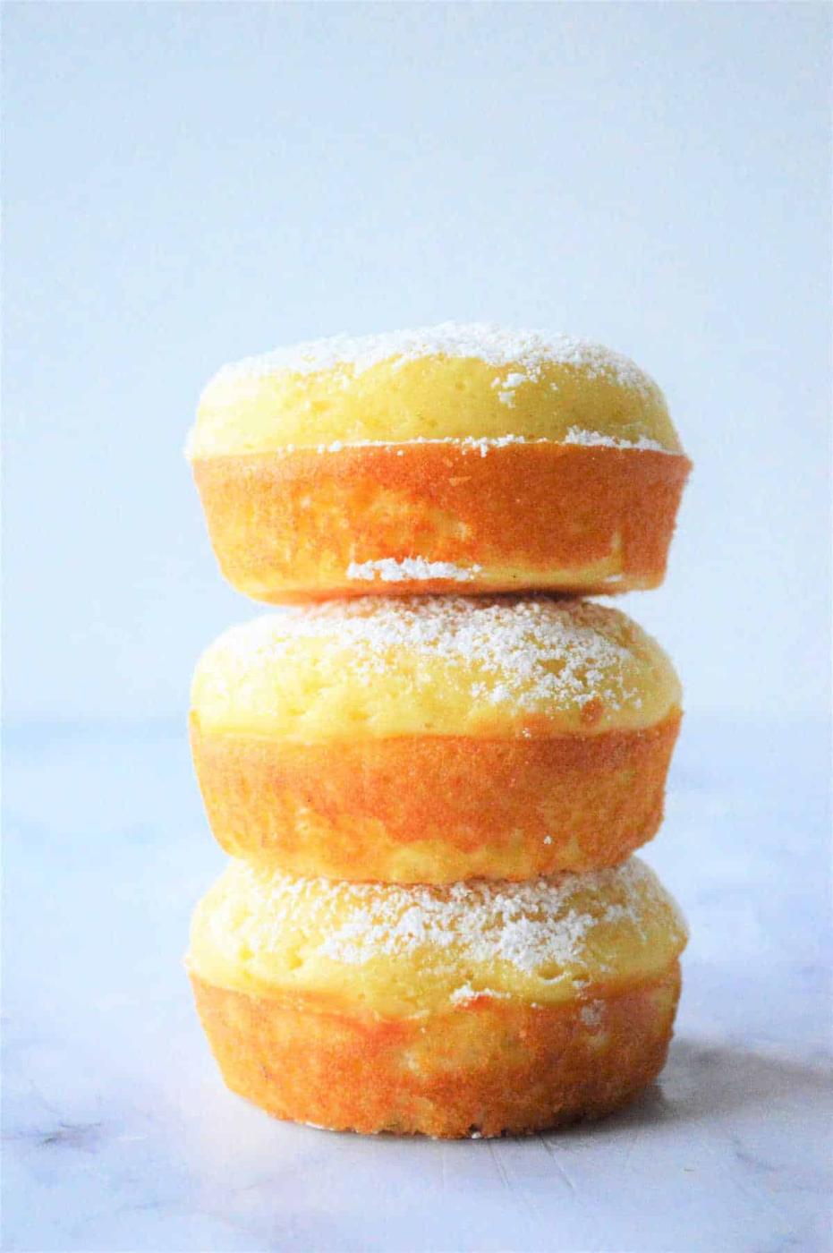 Three stacked lemon fluffy Bisquick muffins, are delicately dusted with powdered sugar on a light background.