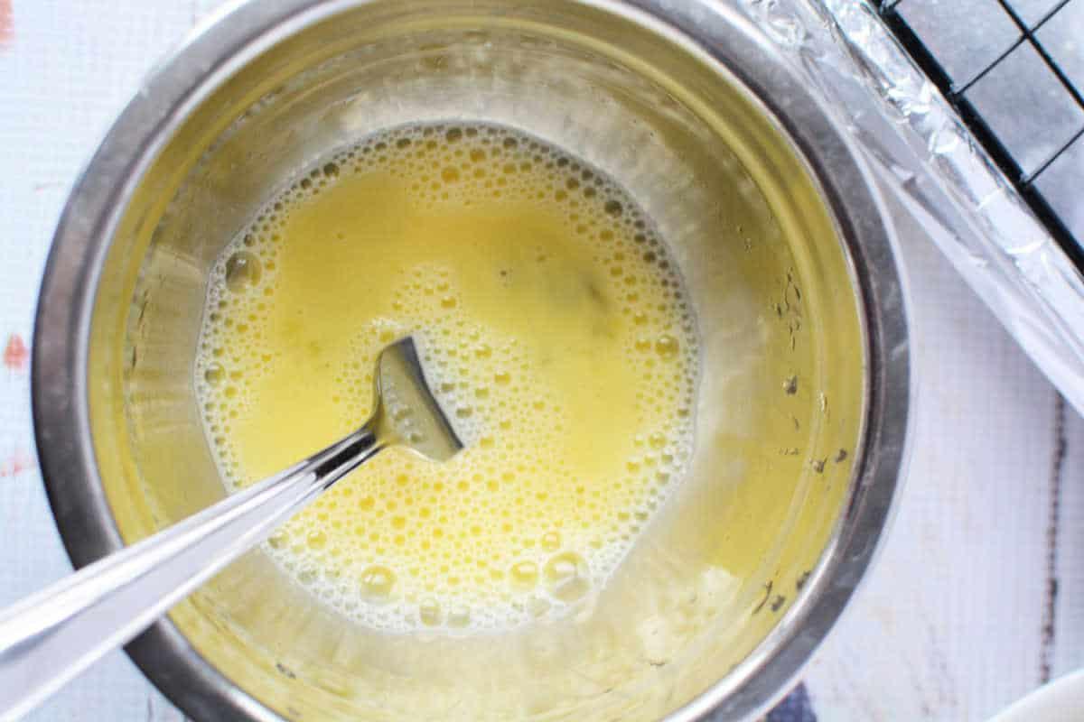 Beaten eggs in a metal bowl with a fork, ready to coat your oven-fried chicken on a light countertop.