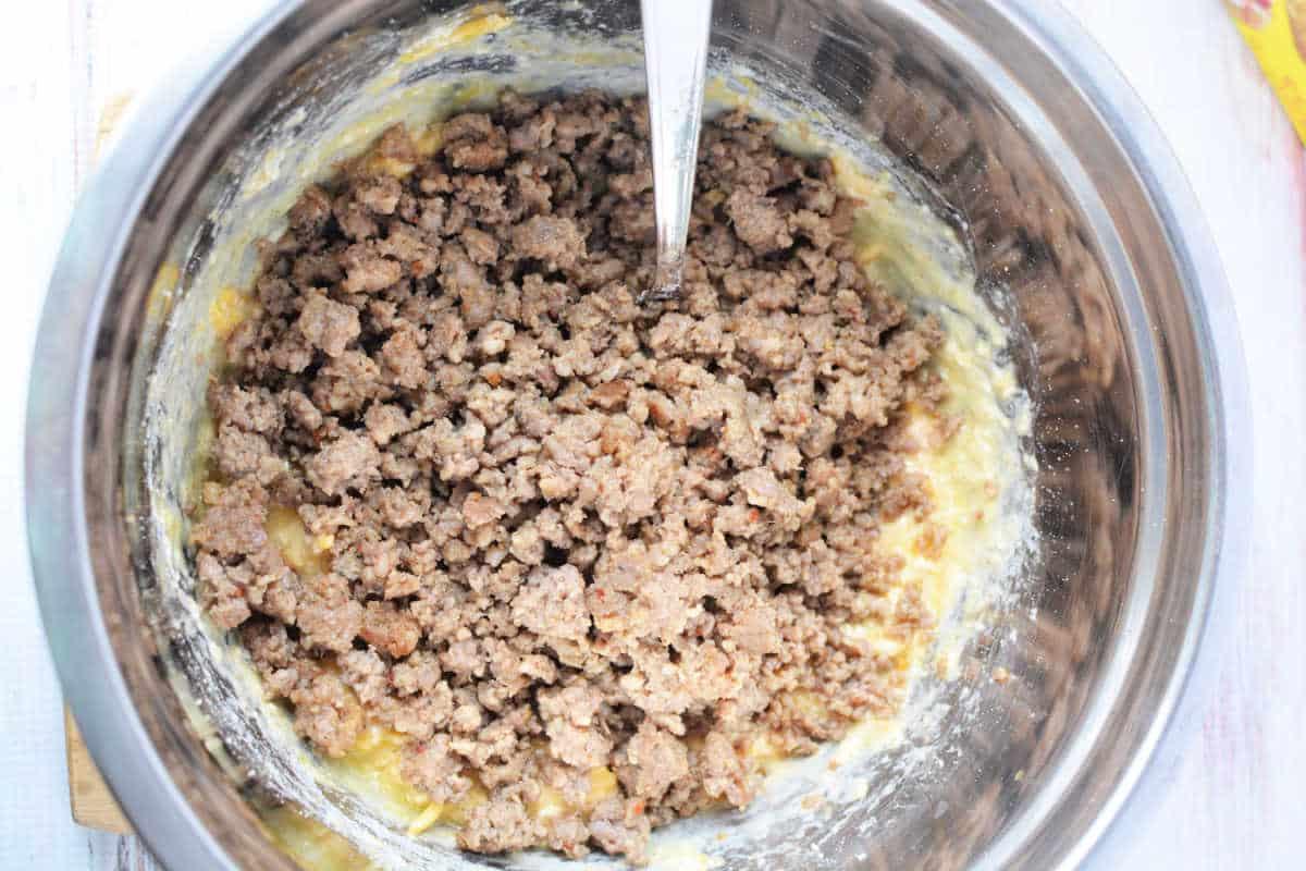 Ground sausage and other ingredients in a metal bowl, stirred gently with a spoon.