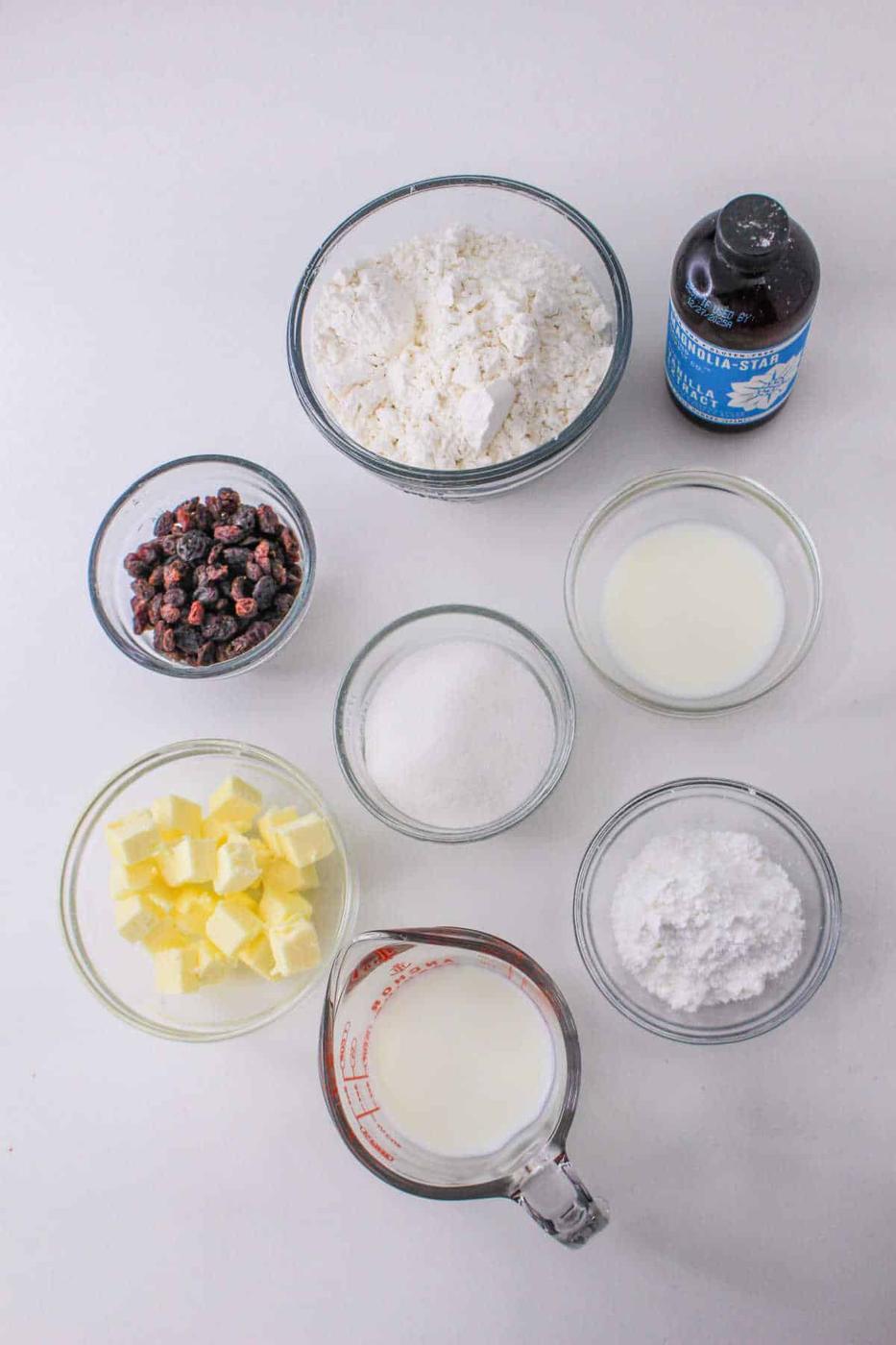 On the table, baking ingredients await their destiny: flour, sugar, butter, milk, dried berries, and vanilla extract mingle in bowls. Nearby sits a box of Bisquick for crafting scones dusted with powdered sugar.