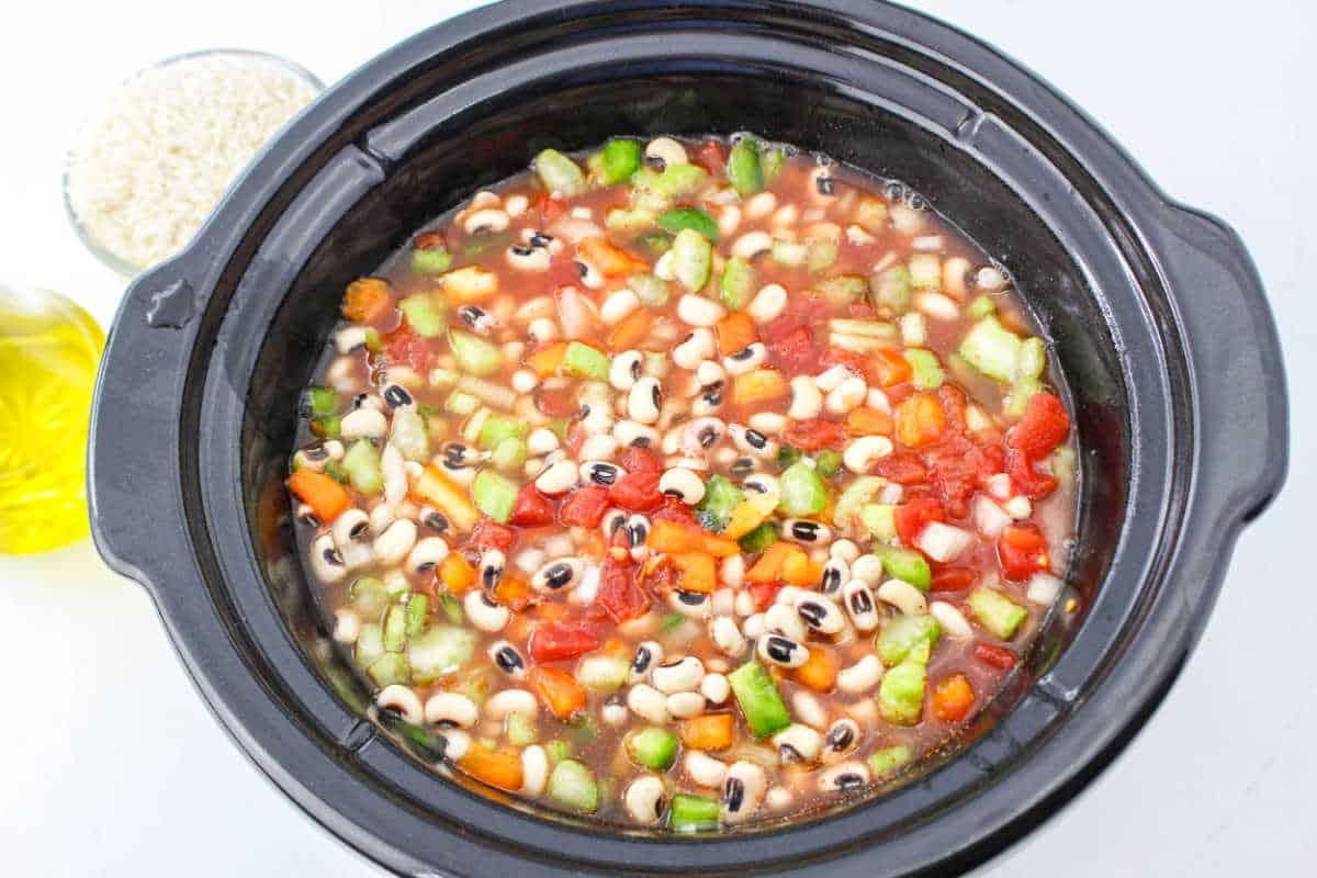 A slow cooker filled with black-eyed peas, diced tomatoes, carrots, celery, broth, and ready for cooking—just add rice to create a comforting Black Eyed Peas and Rice dish.