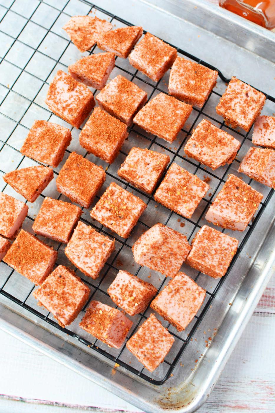 Cubes of pink candy coated with chili powder on a cooling rack over a metal baking sheet, reminiscent of Bologna Burnt Ends in their bold flavor and unique presentation.