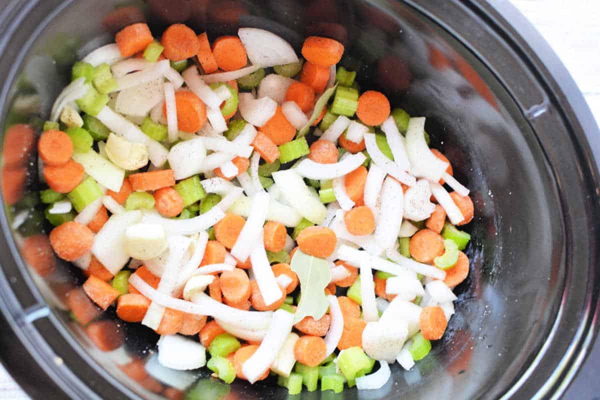 Chopped carrots, celery, onions, and potatoes simmer in a savory broth recipe within the slow cooker.