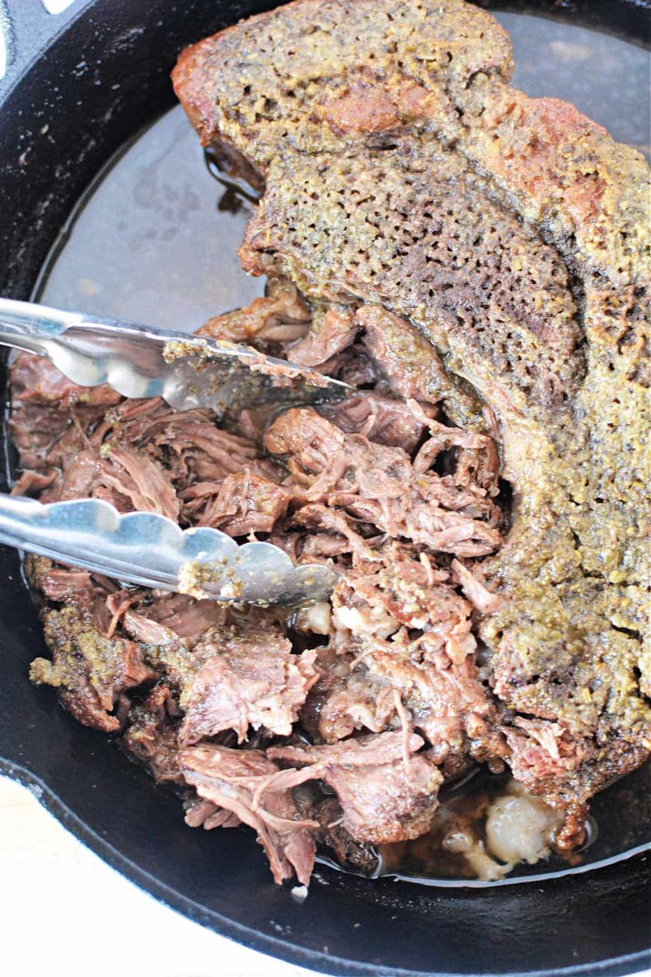 Boneless pot roast shredded with tongs in a cast iron skillet.