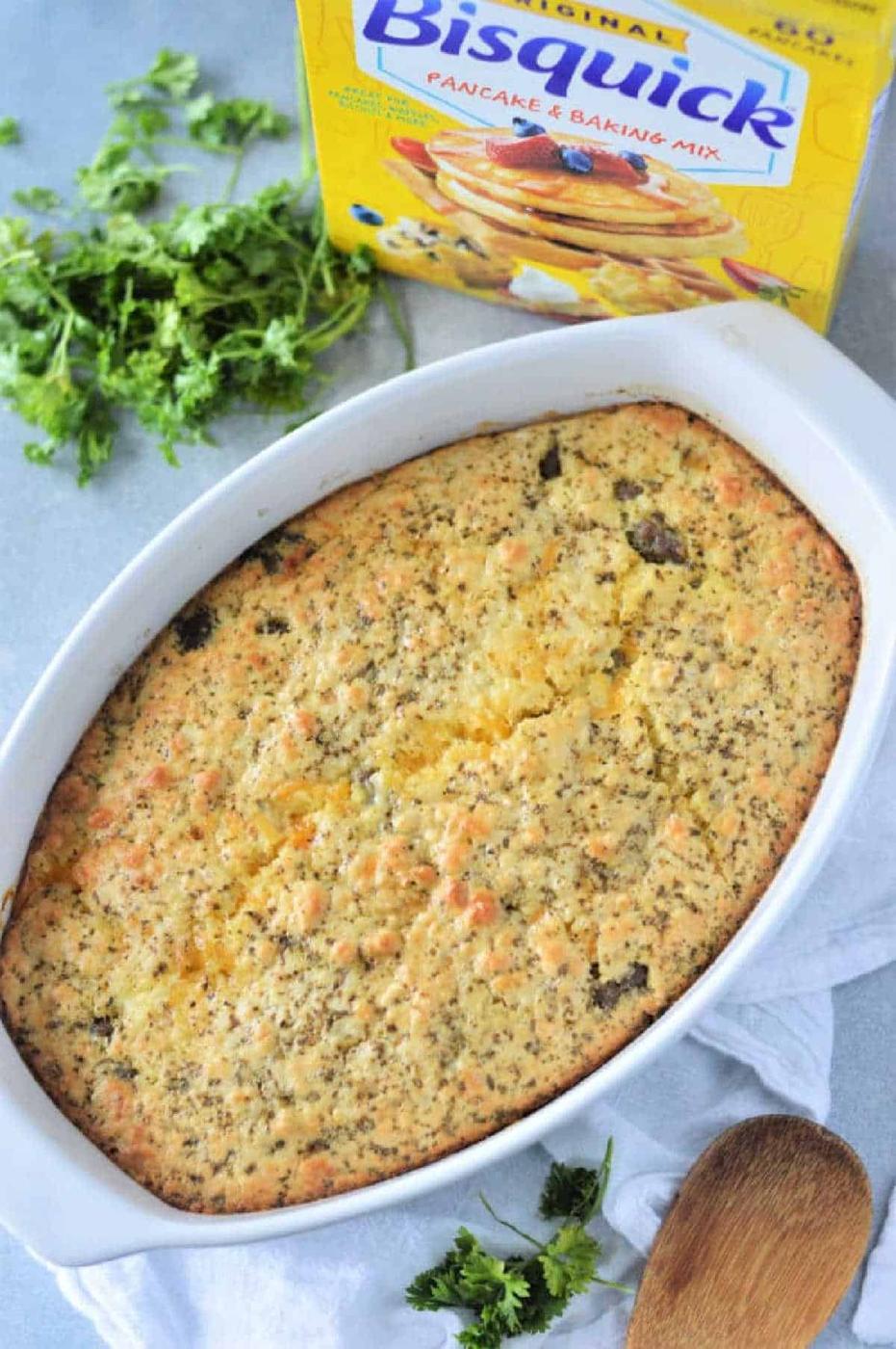 Breakfast Casserole with Bisquick baked in a white dish, with a Bisquick box and fresh parsley nearby on a light surface.