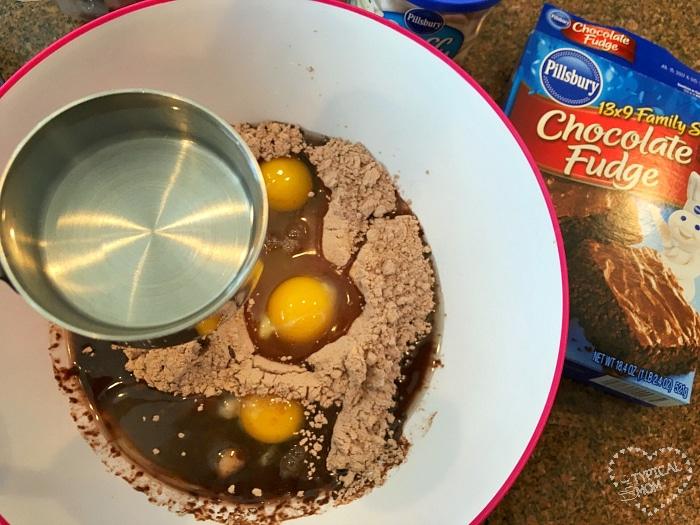 A bowl sits ready as chocolate fudge cake mix, eggs, and water are added to create a decadent treat. The Pillsbury Chocolate Fudge box stands nearby, hinting deliciously at the possibility of brownie waffles in your future.
