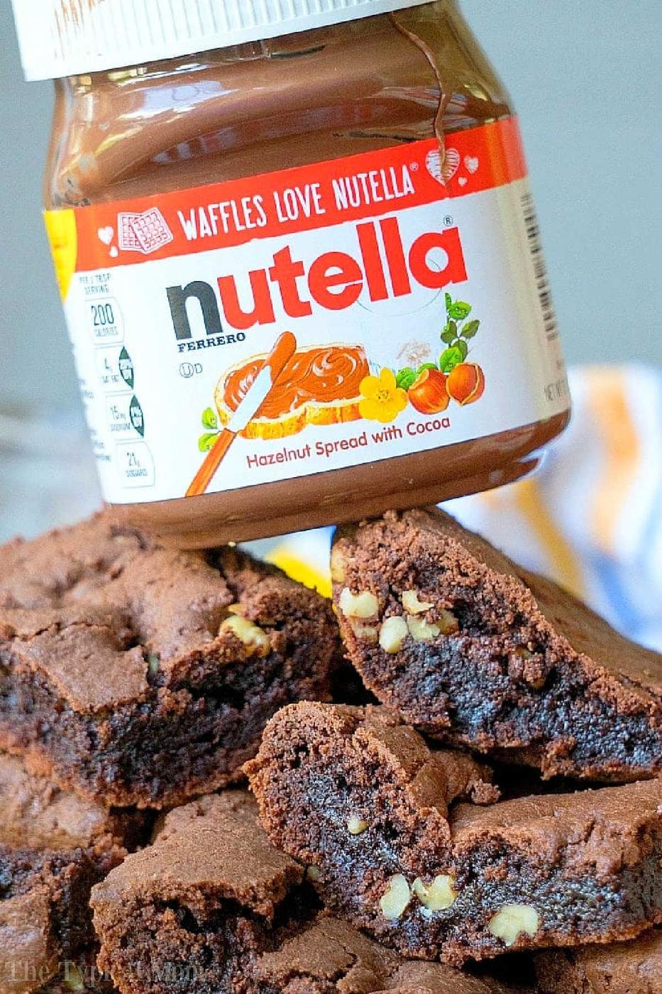 A jar of Nutella above stacked chocolate brownies from cake mix devils food, with visible nuts inside.