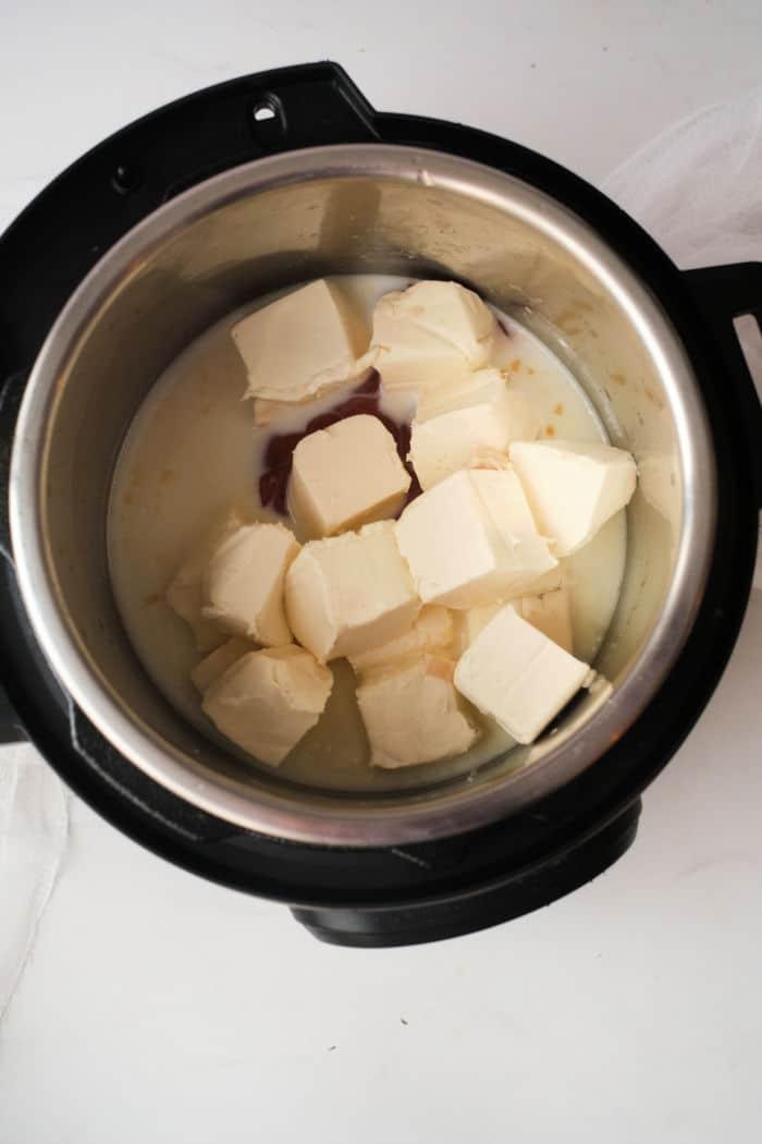 Cubes of cream cheese in a metal pot, partially melted alongside a creamy buffalo chicken dip liquid.
