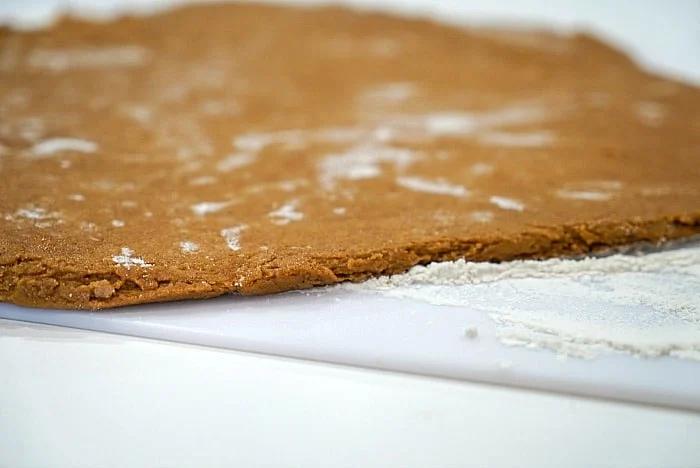 Rolled-out dough for gingerbread cookies, rests on a floured surface, ready for baking.
