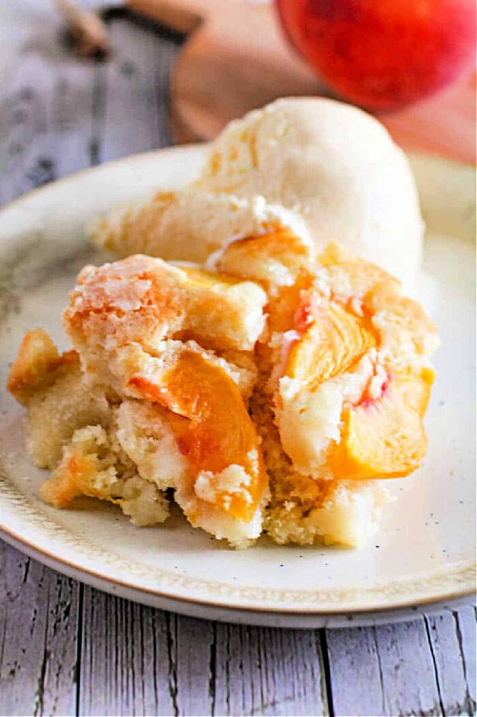 A plate with Peach Dump Cake with Fresh Peaches and a scoop of vanilla ice cream sits on a wooden table.