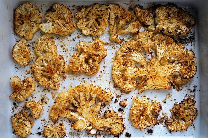 Sliced, roasted cauliflower steak seasoned with spices and cooked to perfection in the air fryer on a white baking tray.