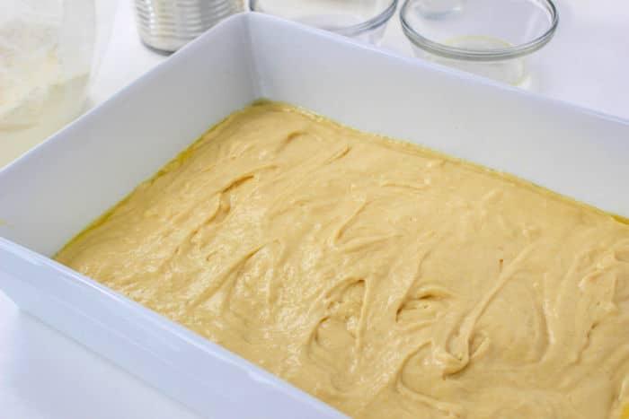 Yellow cake batter spread evenly in a white rectangular baking dish, ready to be baked into a delicious Cherry Coffee Cake.