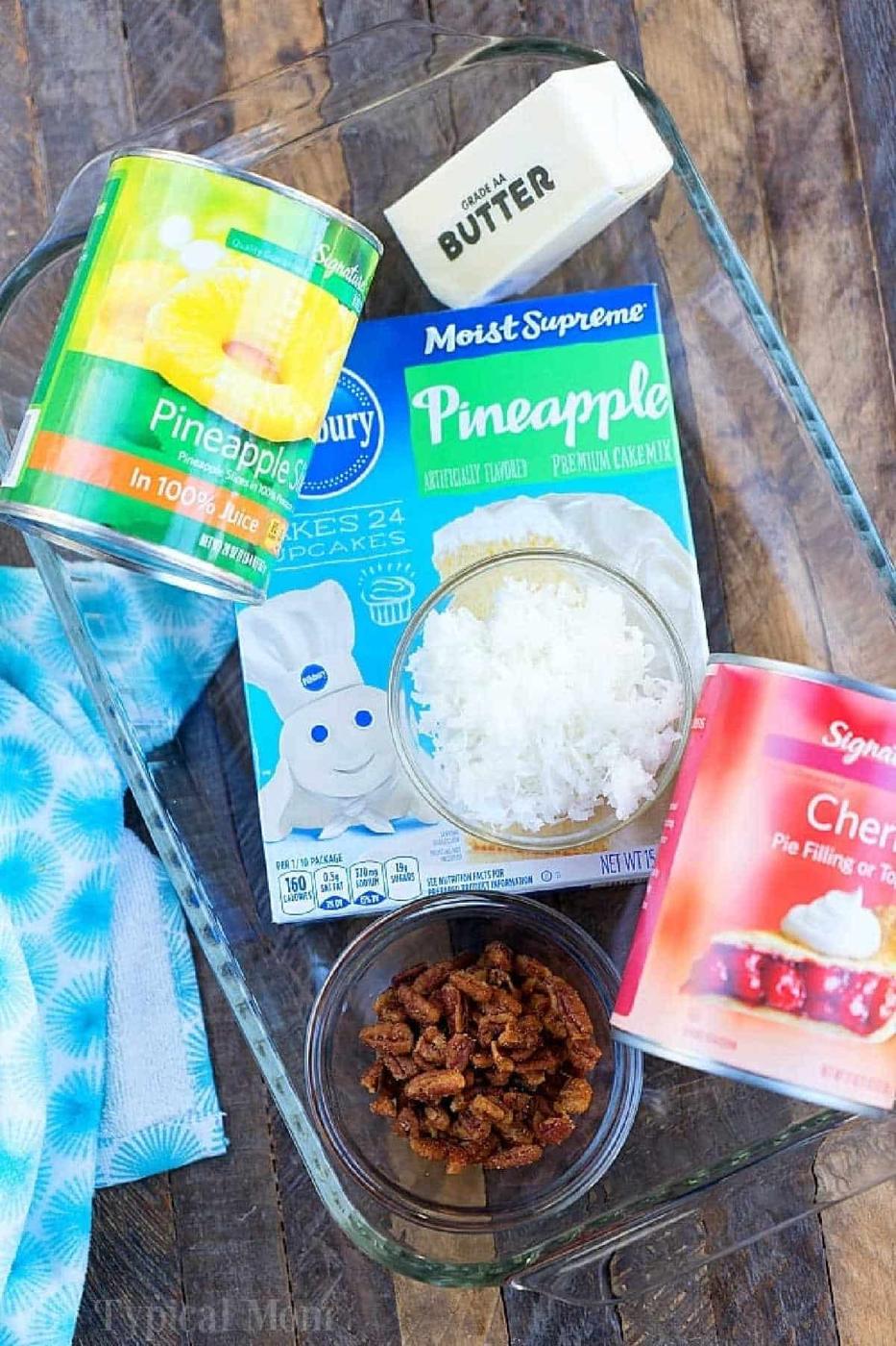 Glass dish layered with canned pineapple, cherry pie filling, cherry pineapple dump cake with white cake mix, shredded coconut, butter, and chopped pecans.
