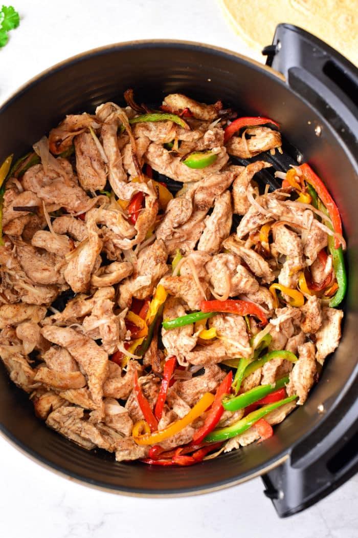 A pan filled with cooked chicken strips and vibrant red, green, and yellow bell peppers creates the perfect base for delicious Chicken Fajita Tacos.