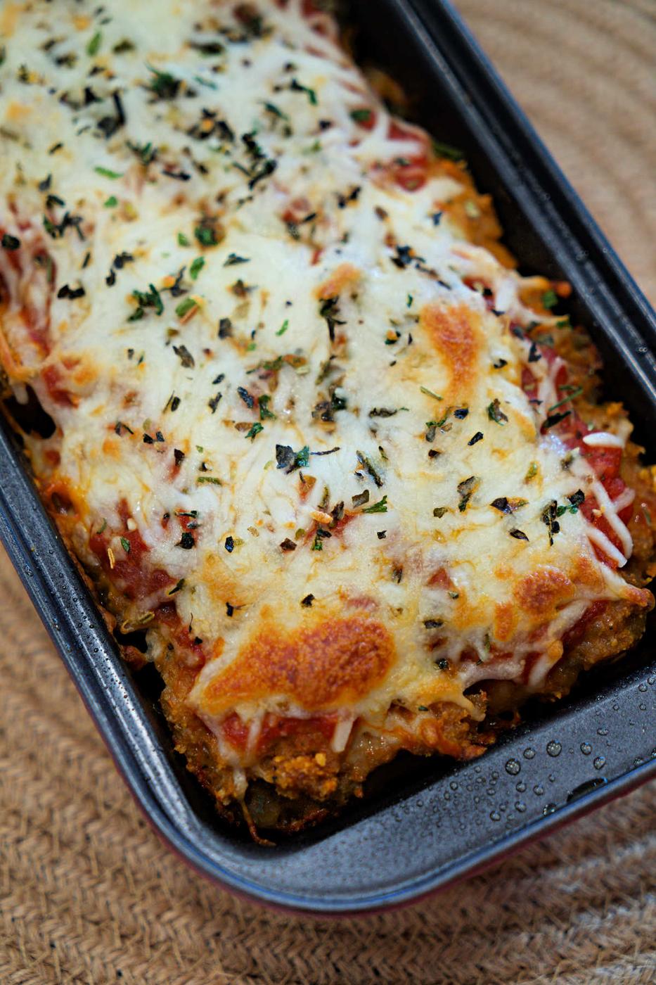 Baked Chicken Parmesan Meatloaf casserole topped with melted cheese and herbs in a rectangular dish on a woven placemat.