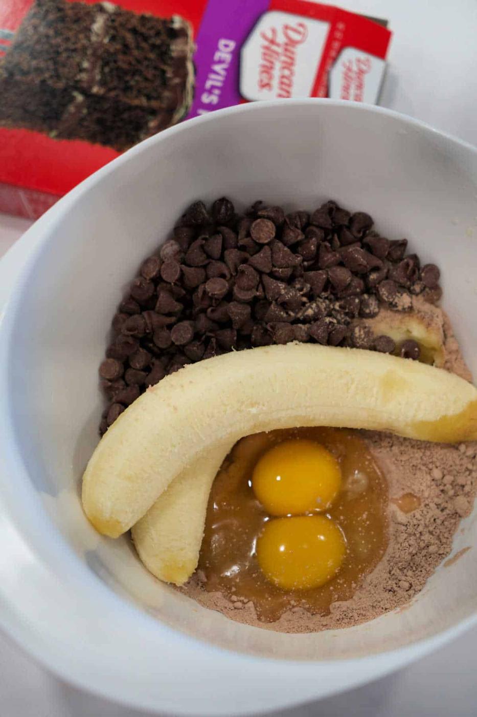 A mixing bowl with eggs, banana, chocolate chips, and cake mix—perfect for whipping up easy chocolate banana bread; a cake mix box sits in the background.
