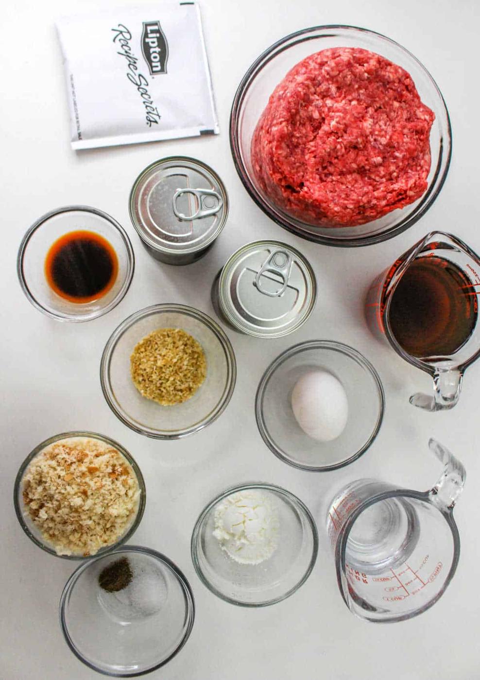 Top view of raw ground beef, seasonings, sauces, egg, breadcrumbs, and canned soup ingredients on a white surface—perfect for making a classic Chopped Steak Recipe.