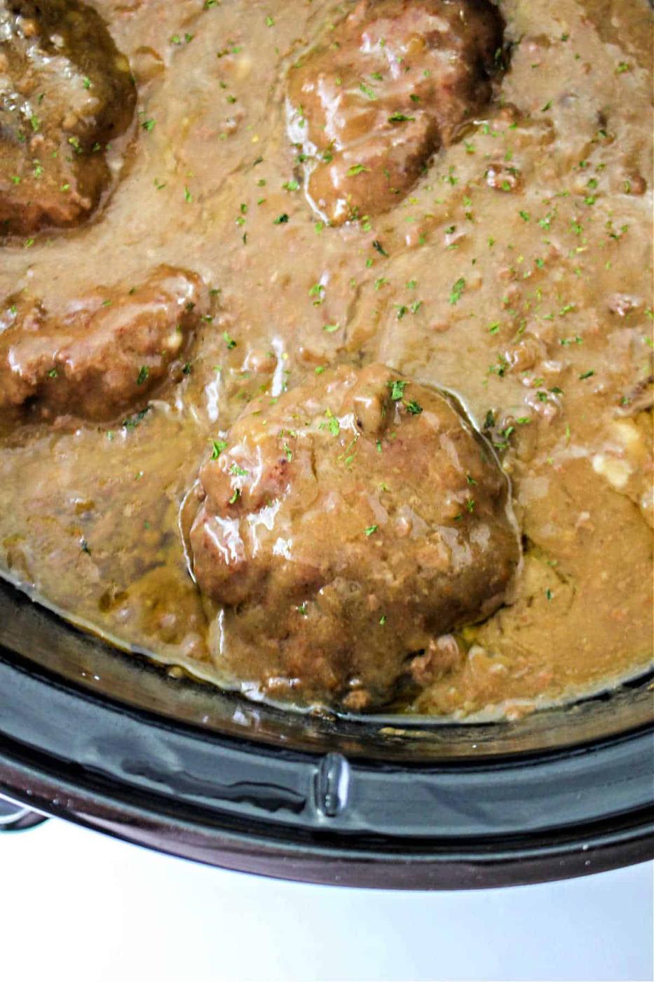 Savor the aroma of chopped steak simmering in rich brown gravy inside a slow cooker, reminiscent of a classic chopped steak recipe.