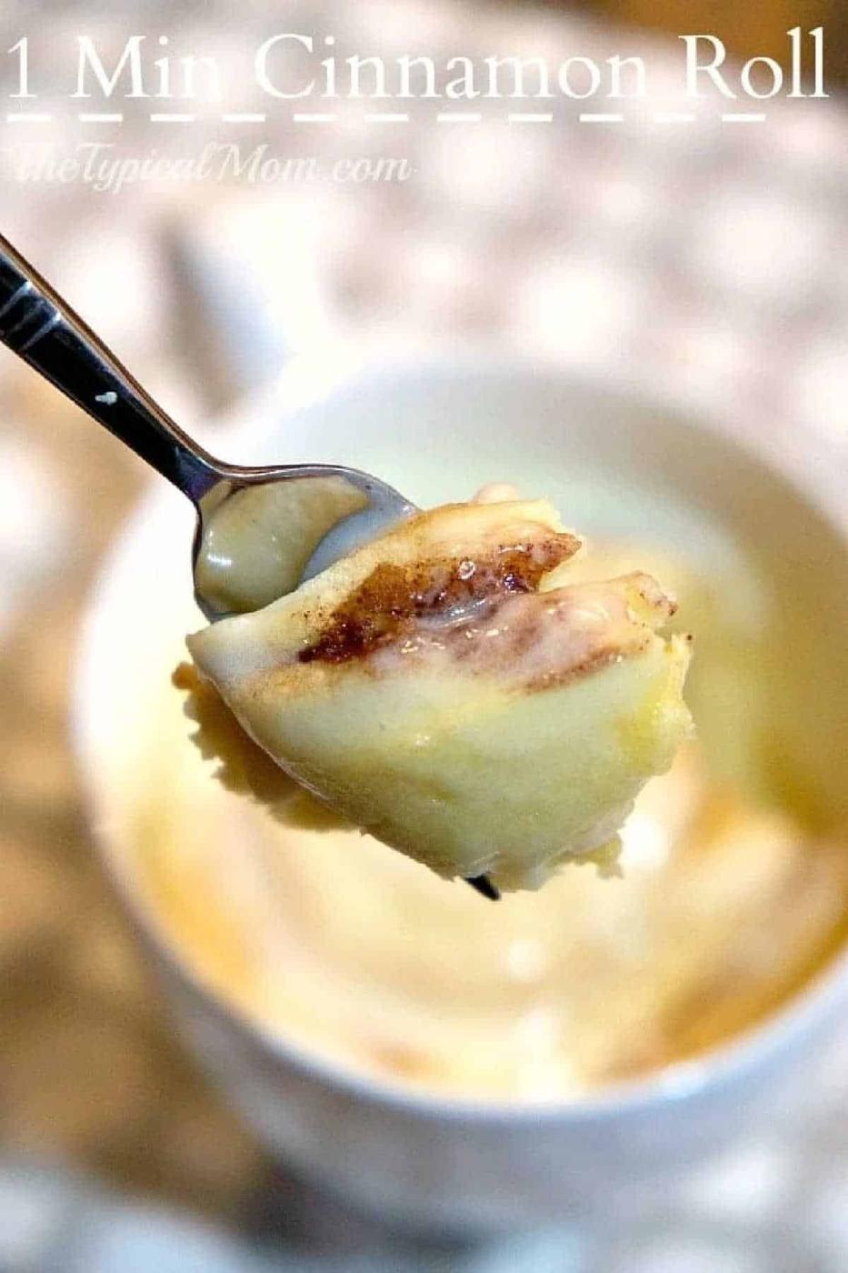A fork holds a bite of cinnamon roll above a mug, with icing visible on the roll—perfect for enjoying a warm cinnamon roll in a mug.