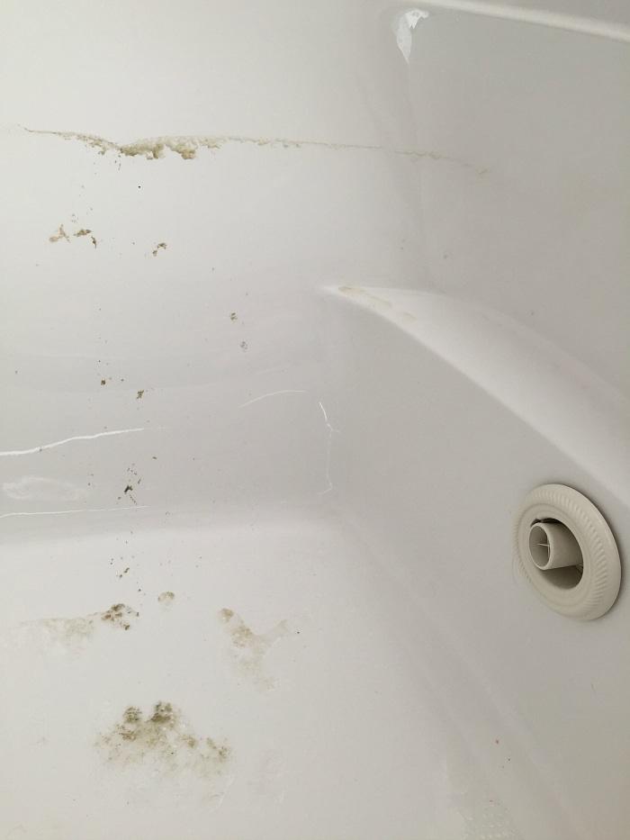 A close-up image of a white bathtub with noticeable mold and grime buildup around the edges and surface. The bathtub drain is partially visible in the bottom right corner. This jetted tub has visible dirt and requires thorough cleaning.