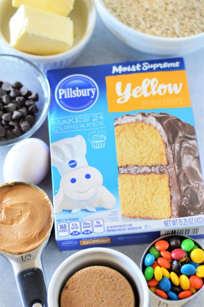 Box of Pillsbury yellow cake mix surrounded by butter, chocolate chips, egg, peanut butter, and candy—perfect for making delicious Cookie Bars From Cake Mix.