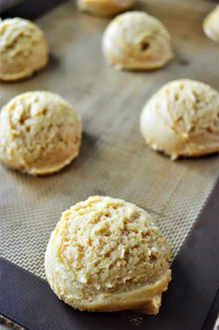 Scoops of raw cookies made with cake mix are spaced out on a baking sheet lined with a silicone baking mat.