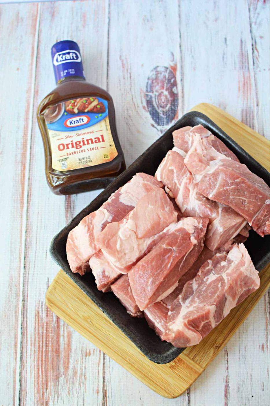 Raw boneless pork ribs rest on a black tray beside a bottle of Kraft Original Barbecue Sauce, perfect for your next pork ribs recipe, all set on a wooden surface.