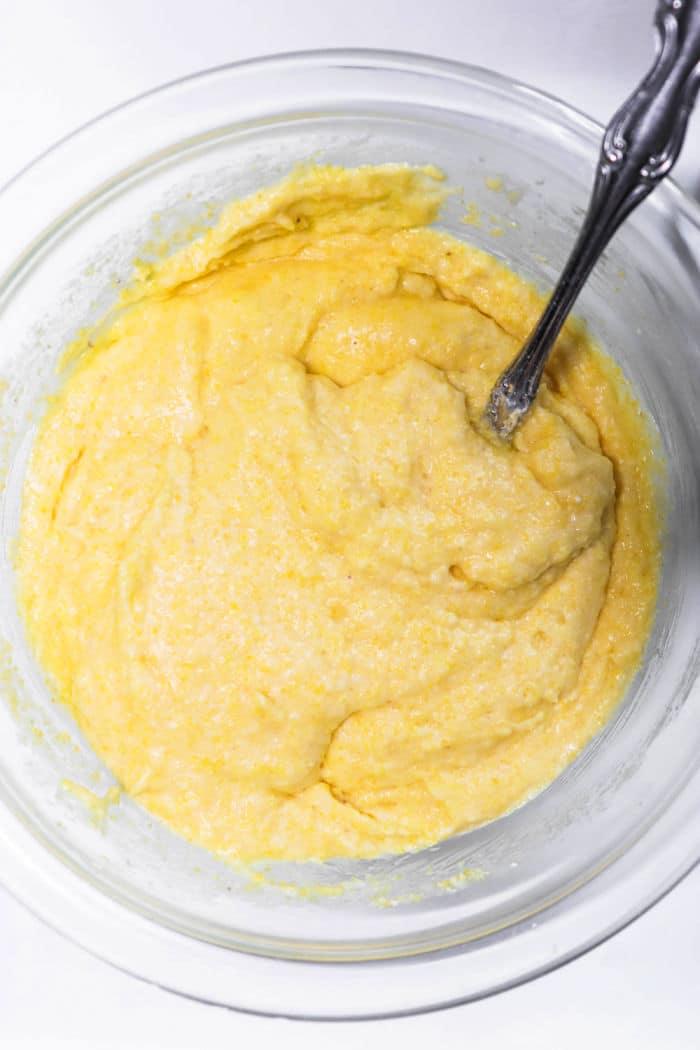 Yellow corn dog bites batter in a glass bowl with a metal spoon.
