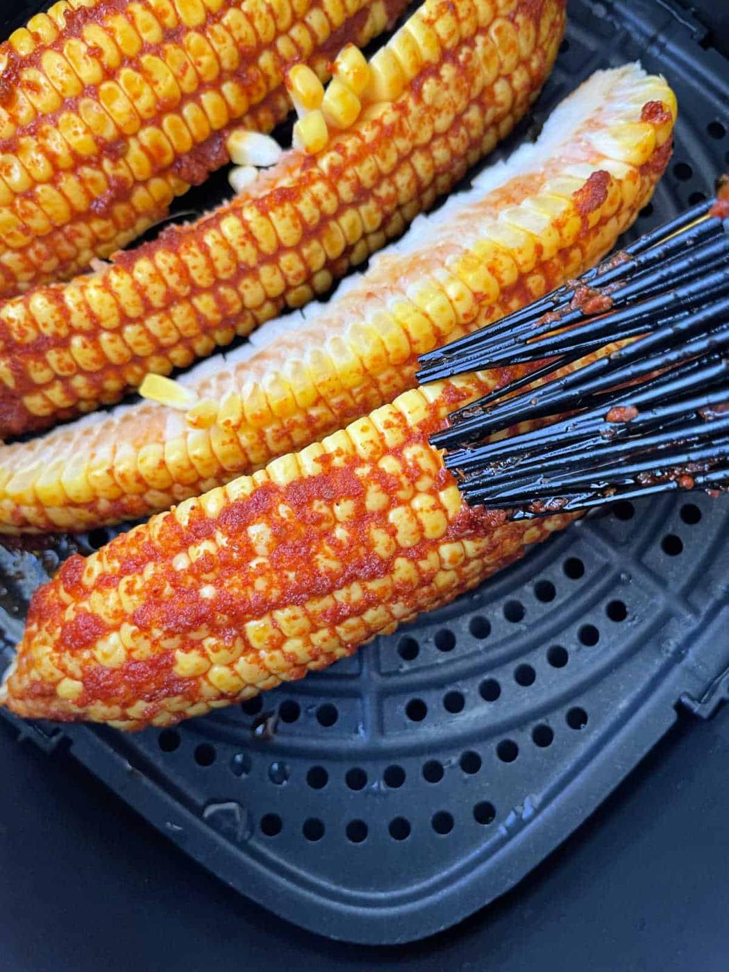 Corn on the cob ribs, brushed with vibrant red seasoning, transforms into a delicious corn ribs recipe as it cooks in a sleek black air fryer basket.