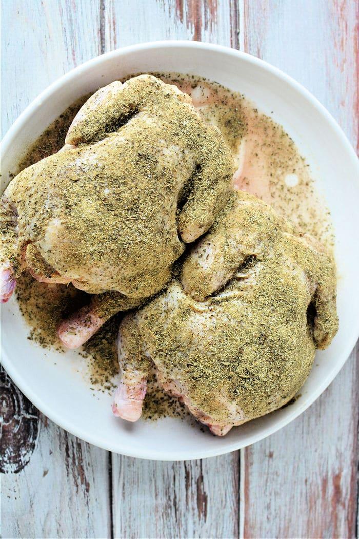 Two raw, seasoned little chickens in a white bowl rest on a rustic wooden surface, ready for their transformation. Wondering about cooking times? Consider how long to cook Cornish hen in an air fryer to achieve crispy perfection.