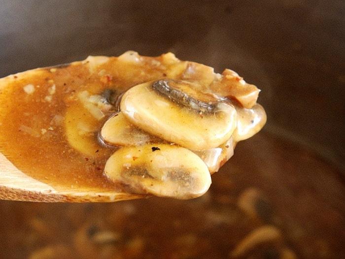 Close-up of mushrooms in a rich brown sauce, reminiscent of Instant Pot Salisbury steak, on a wooden spoon.