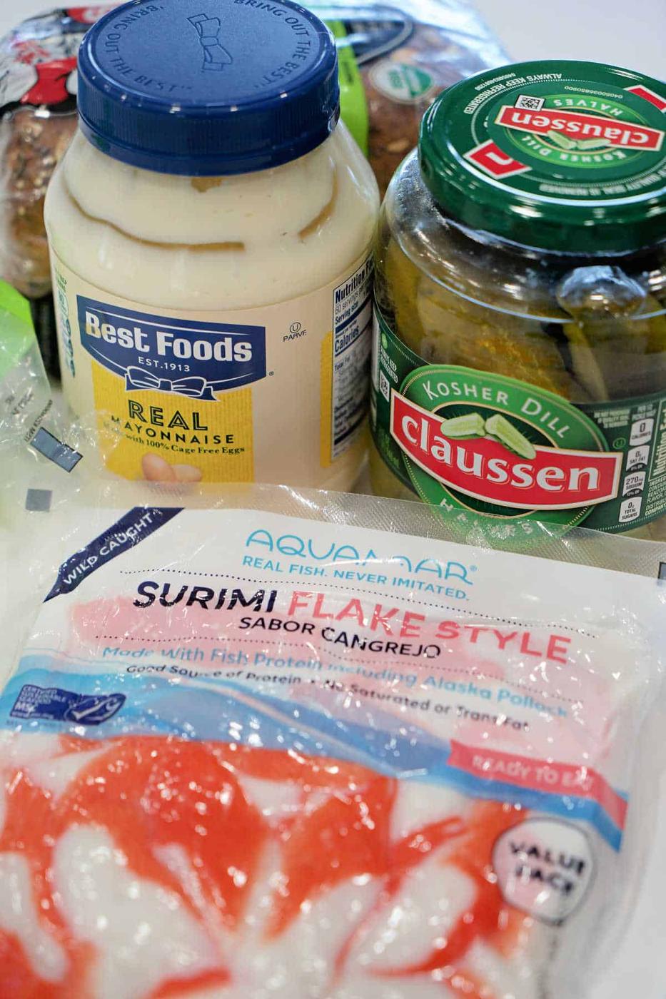 Jars of mayonnaise and pickles with a package of surimi crab sticks on a kitchen counter.