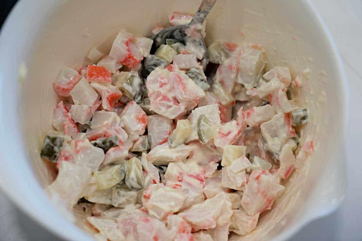A bowl of creamy salad with diced vegetables and imitation crab, mixed with a spoon.