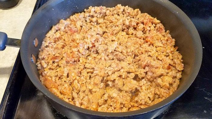 Cooked seasoned ground meat in a black skillet on a stovetop, perfect for adding rich flavor to your favorite crockpot tortellini soup recipe.