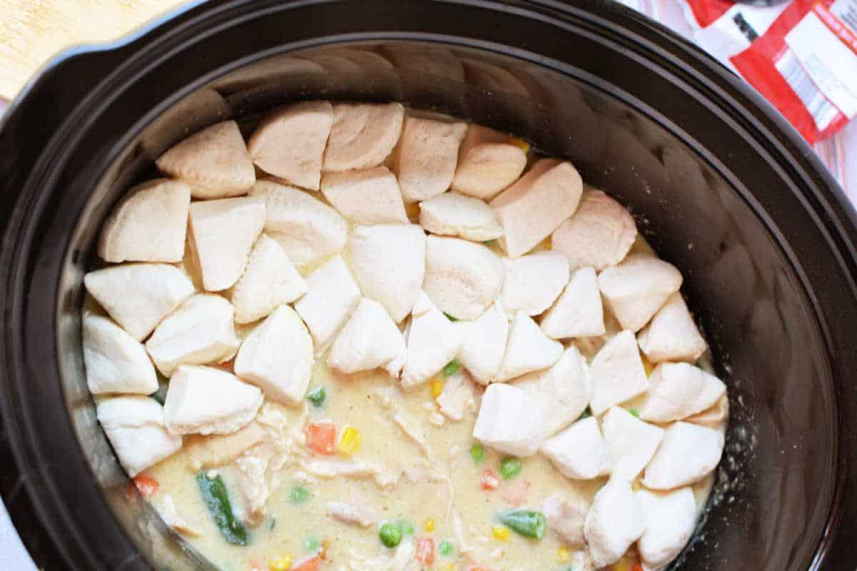 Crockpot Chicken and vegetable stew in a slow cooker, topped with raw biscuit dough pieces arranged in a ring for a delicious twist on classic Chicken Pot Pie.
