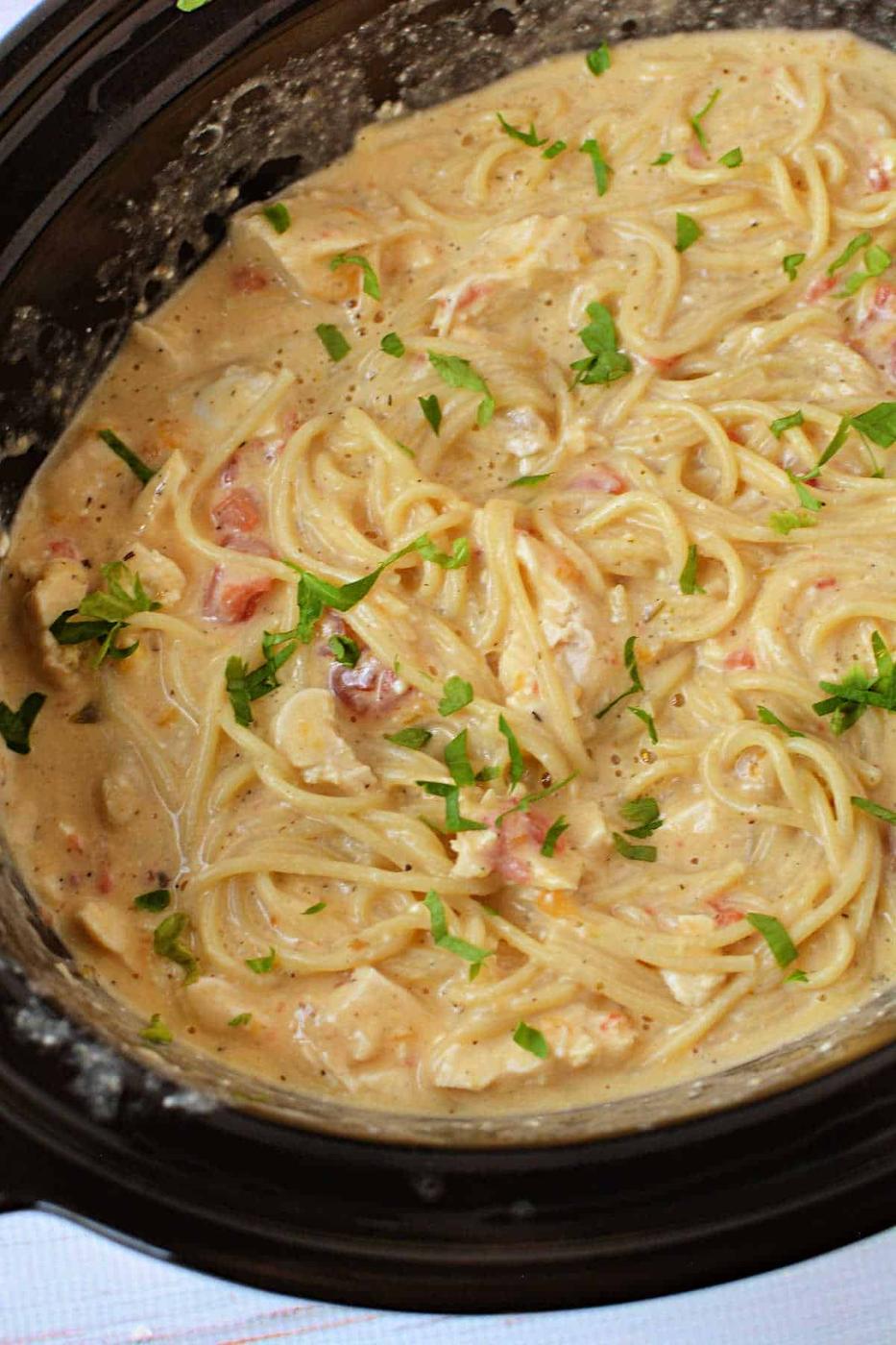 Creamy spaghetti with tomatoes and herbs cooked in a Crockpot, garnished with chopped parsley—a comforting take on classic Chicken Spaghetti made easy.