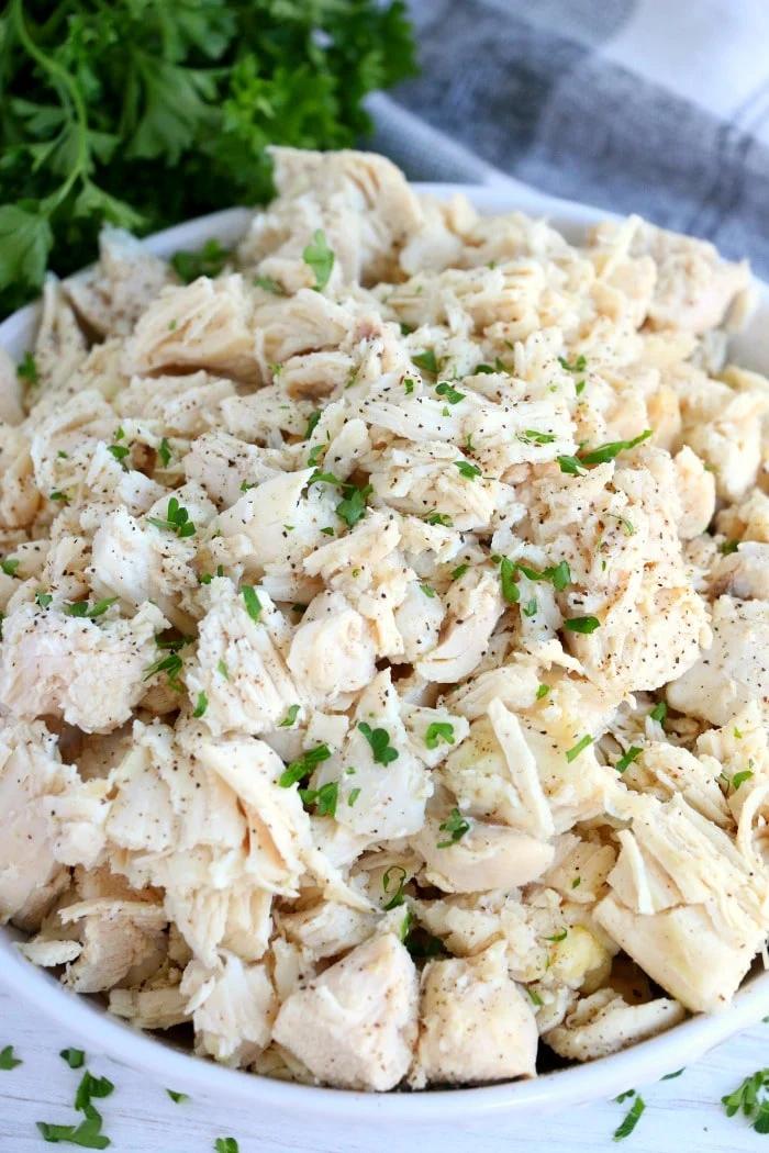 In a white bowl, discover chopped cooked chicken from frozen, seasoned with herbs and pepper in Crockpot