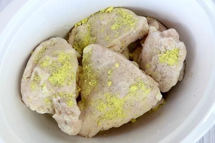 Frozen chicken pieces in a crockpot, generously sprinkled with seasoning, make for an effortless slow-cooked meal.