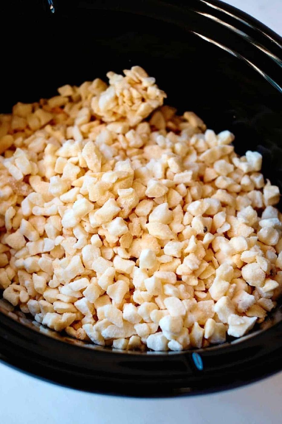 Frozen diced potatoes in a black crockpot, ready to be transformed into classic funeral potatoes.