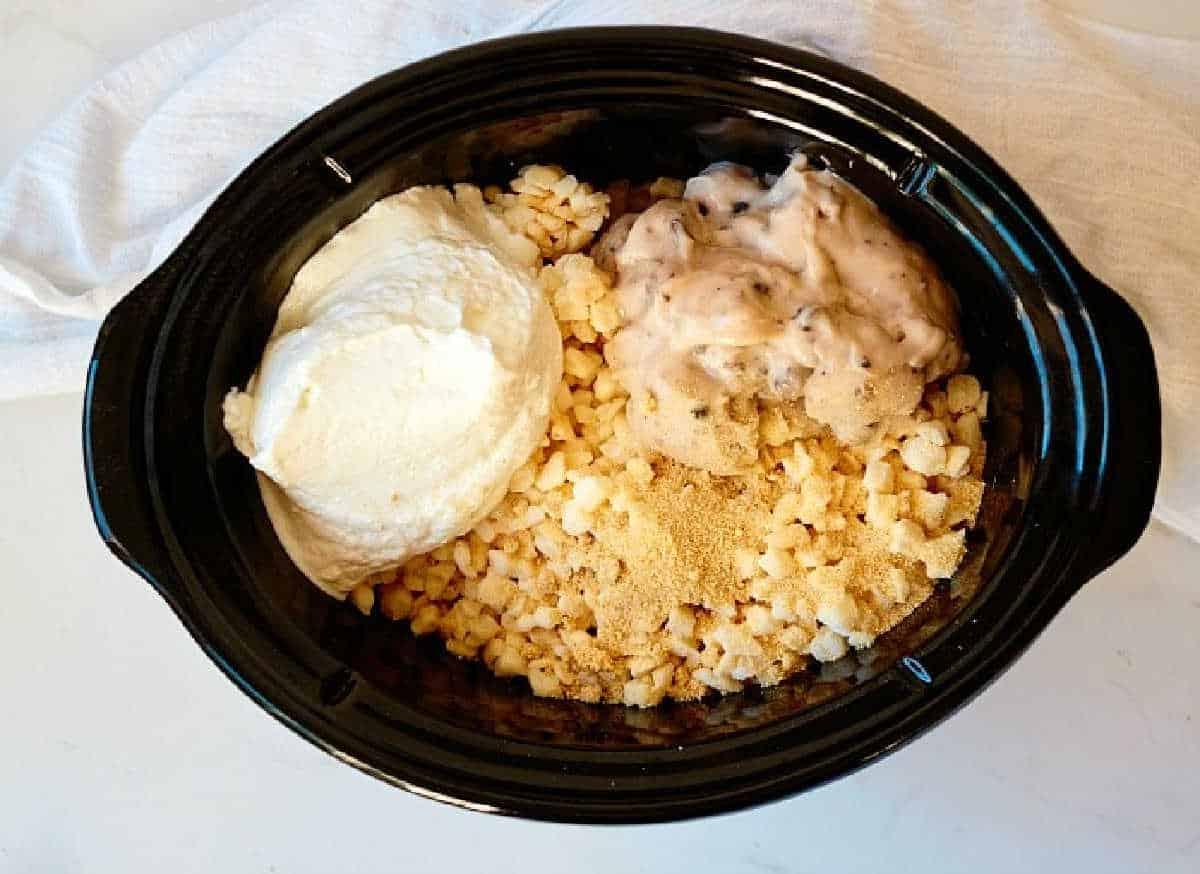 Crockpot funeral potatoes filled with tater tots, creamy sauce, and shredded cheese on a white cloth background.