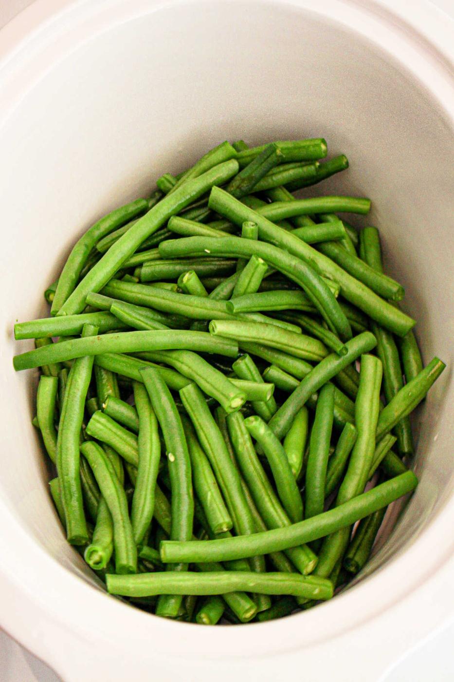 A slow cooker is filled with a pile of raw green beans, freshly cut and vibrant in color, waiting to be prepared or added to your crockpot for a delicious meal.