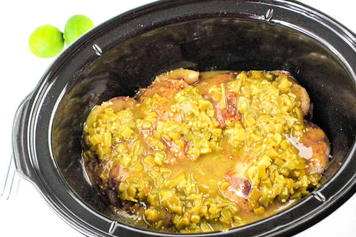 Crockpot chicken breasts topped with green chili sauce, two limes nearby, brings a burst of citrus flavor.