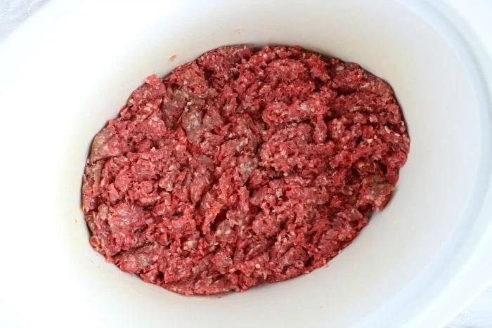 A white slow cooker holds raw ground beef, ready to be transformed into a hearty crockpot meal.