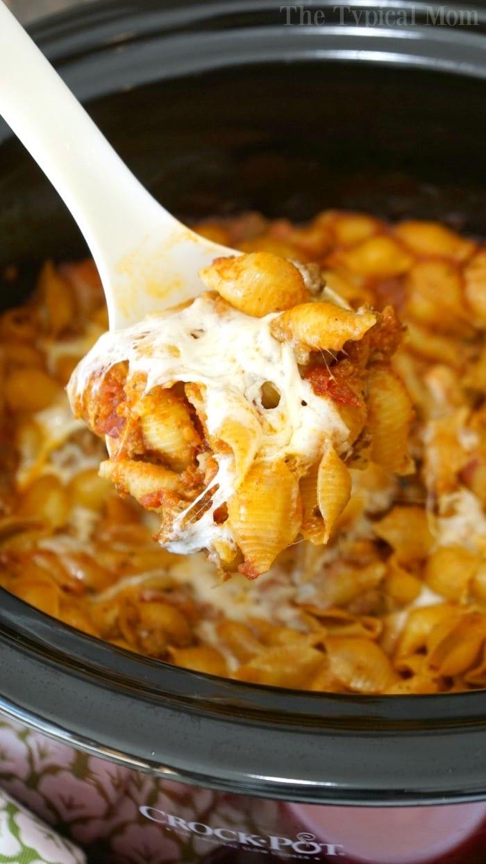 A spoonful of cheesy pasta and sauce is being lifted from a crockpot lasagna, showcasing the delicious layers within.
