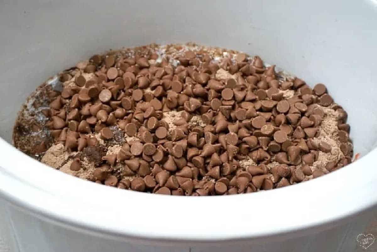 Chocolate chips on top of a layer of dry ingredients in a white crockpot, ready to become a rich and gooey crockpot lava cake with cake mix.