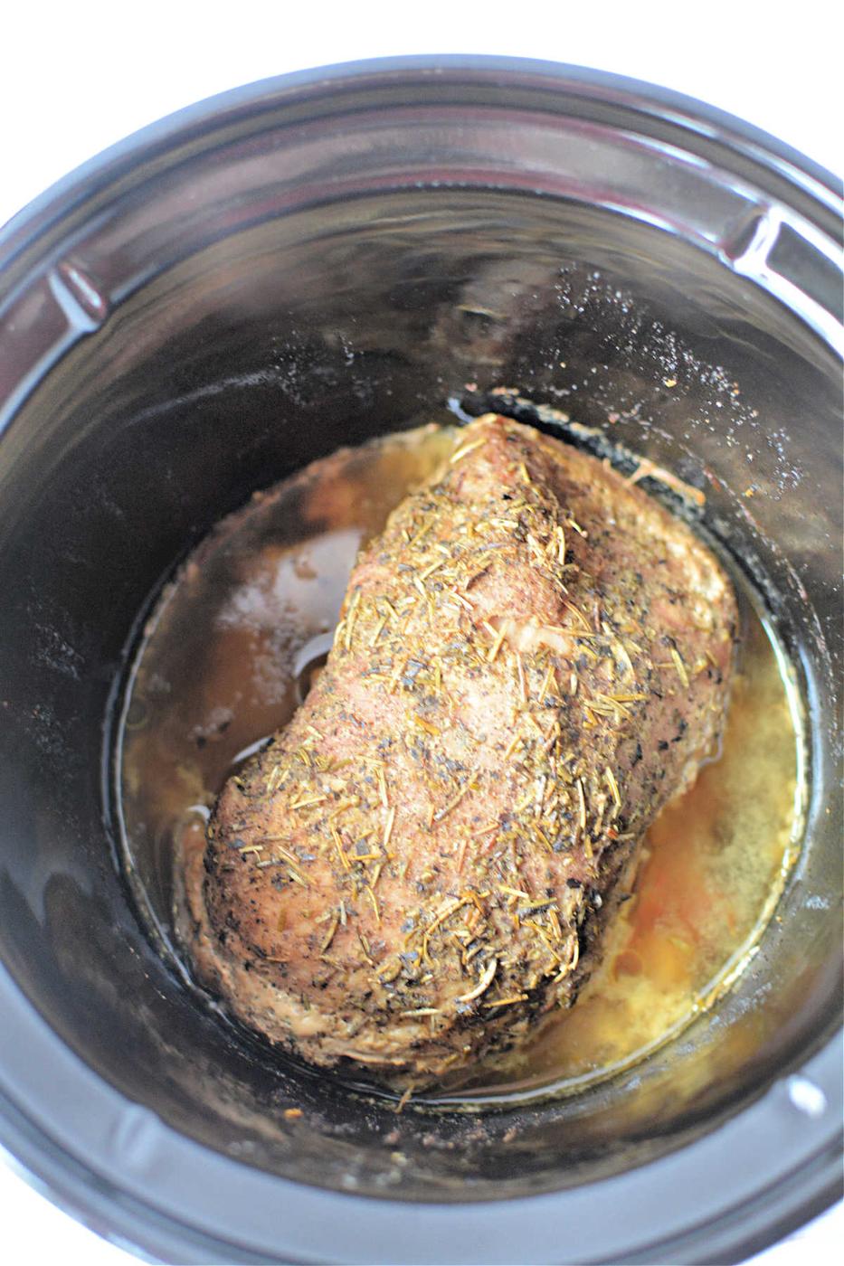 A seasoned Porketta Roast is cooking slowly, melding flavors with its rich, savory juices.